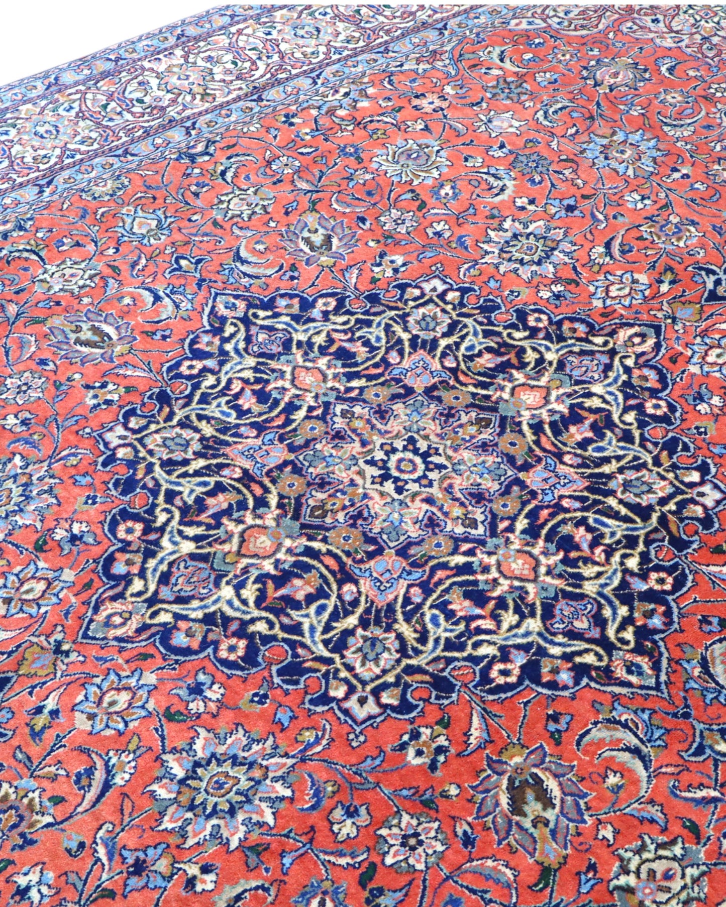 Tappeto persiano Saurk 345x240 cm, fondo rosso corallo con medaglione blu e cornice floreale chiara, annodato a mano in lana vegetale.