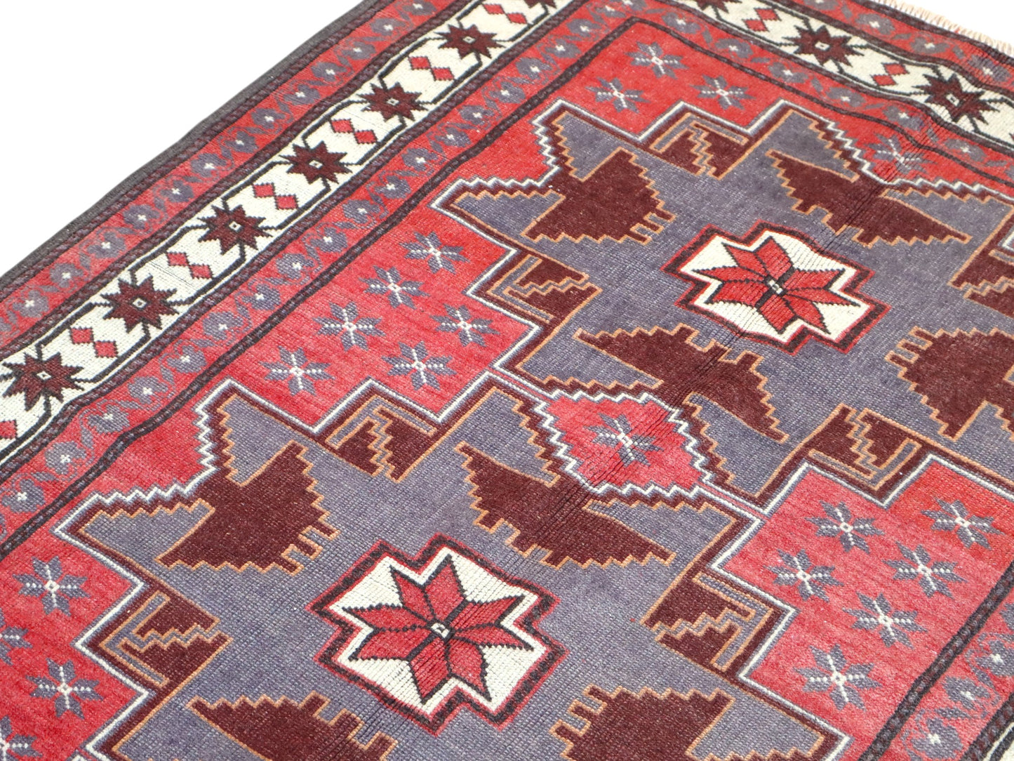 Tappeto Kazak 181x113 cm con motivo geometrico a stelle in rosso, blu e beige, annodato a mano con lana pregiata e ordito in cotone robusto.