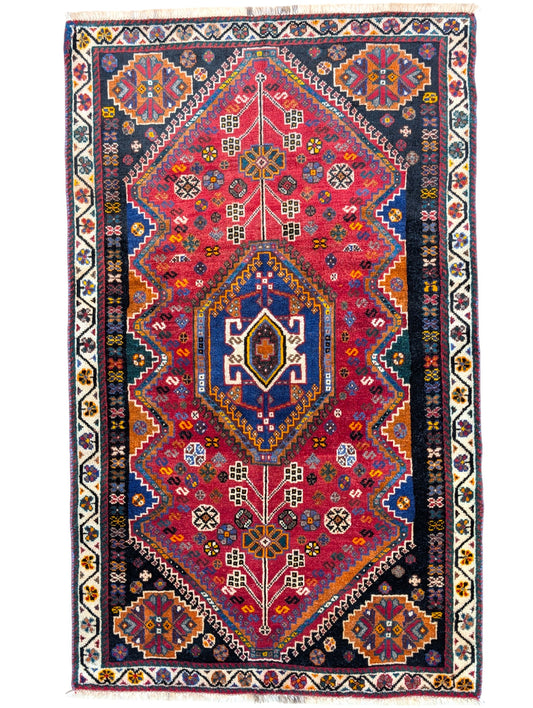 Tappeto Shiraz in rosso melograno con motivi geometrici e stilizzati, evocante un giardino persiano. Annodato a mano con lana e colori vegetali naturali in Persia.