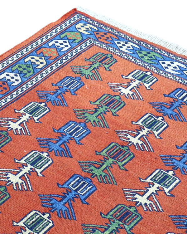 Tappeto Kilim 181x130 cm con motivi geometrici e figure stilizzate in blu, verde e rosso su fondo arancione e bordura decorata.