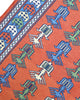 Tappeto Kilim 181x130 cm con motivi geometrici e figure stilizzate in blu, verde e rosso su fondo arancione e bordura decorata.