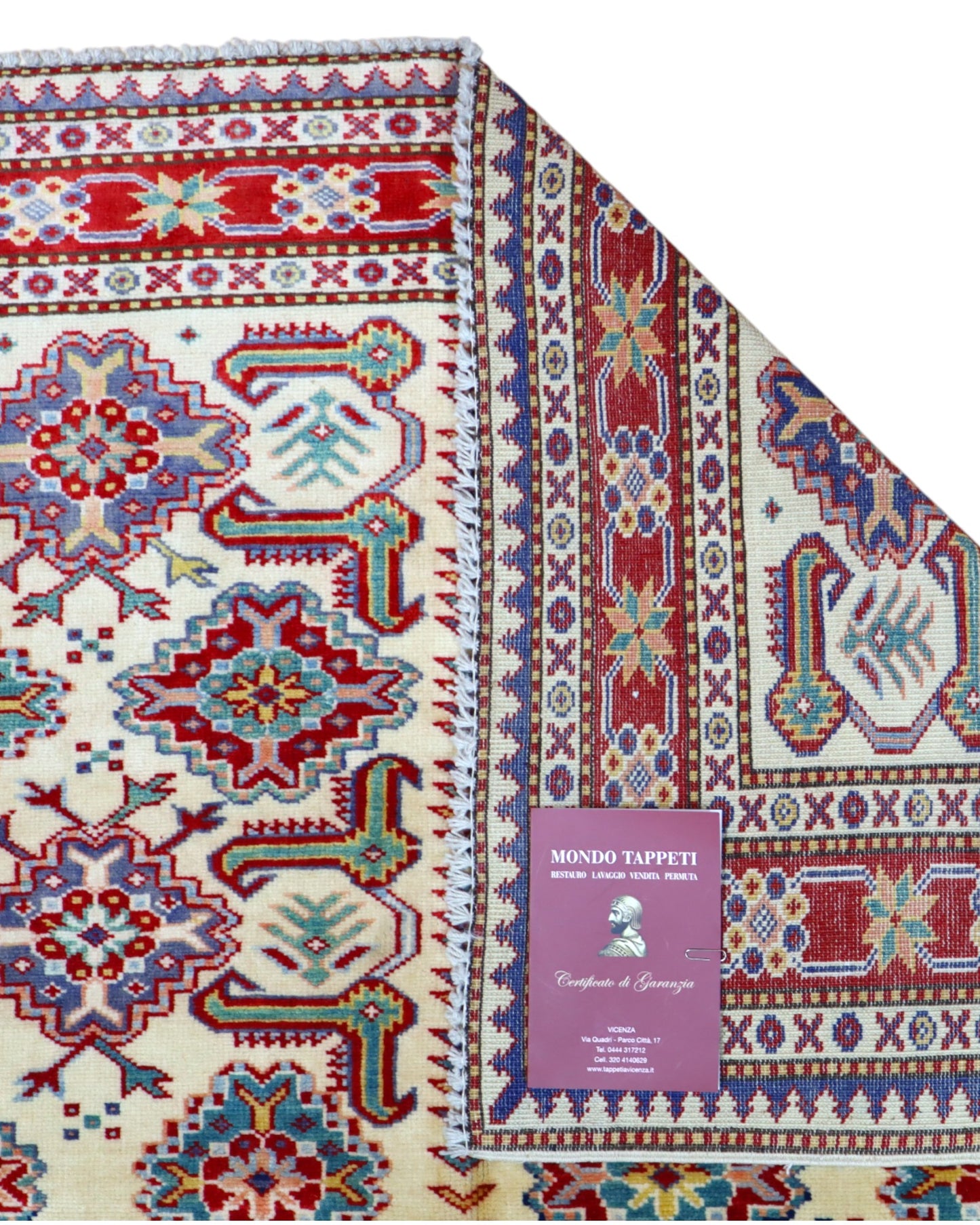 Tappeto Shirvan 165x122 cm con motivi geometrici e floreali in rosso, blu, verde e crema su fondo beige.