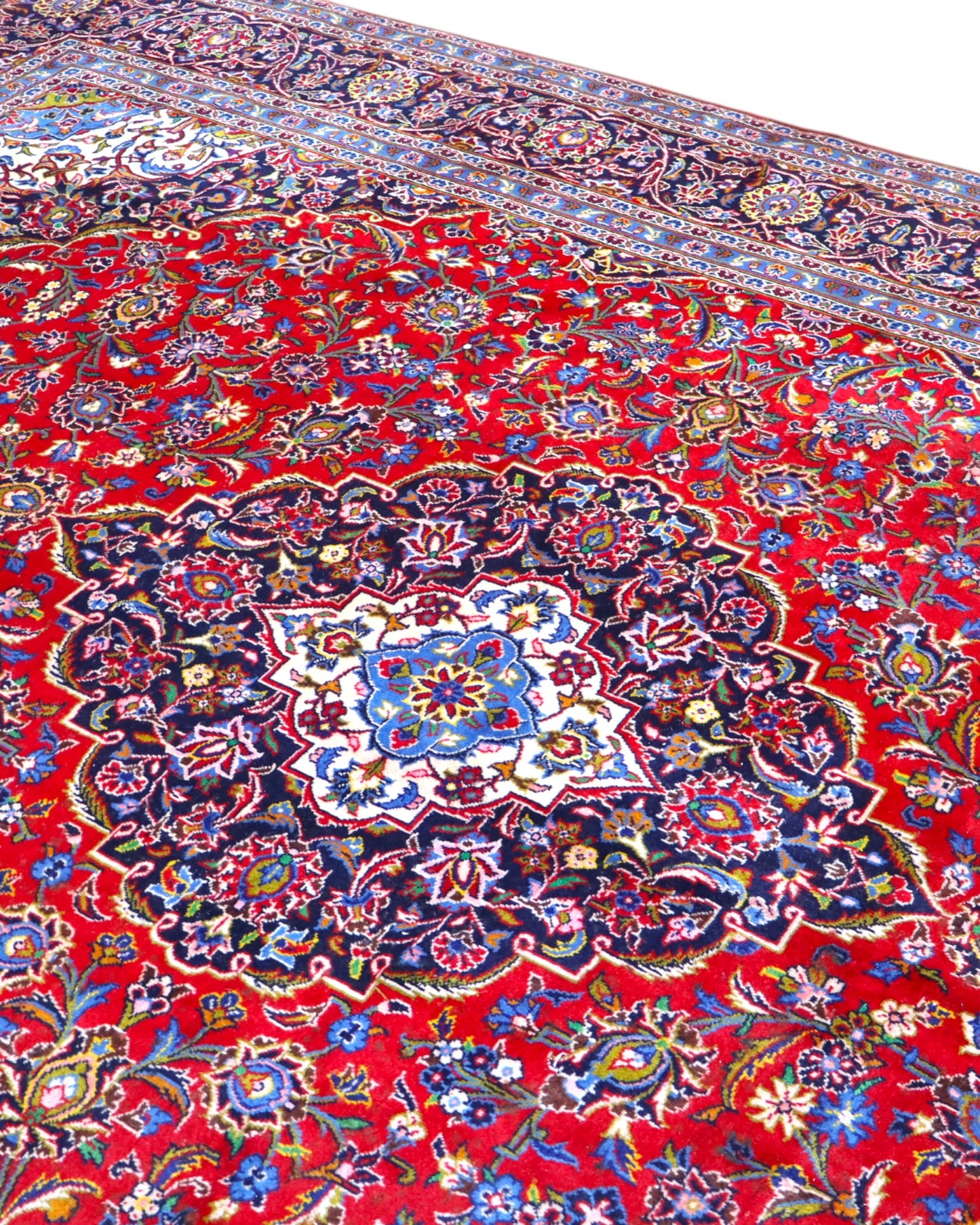 Tappeto persiano Kashan 402x297 cm, fondo rosso con medaglione centrale blu e avorio, annodato a mano in lana vegetale.