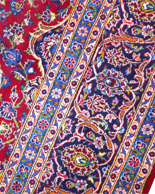 Tappeto persiano Kashan 400x290 cm, fondo rosso con medaglione centrale blu e avorio, cornice scura floreale, annodato a mano in lana vegetale.