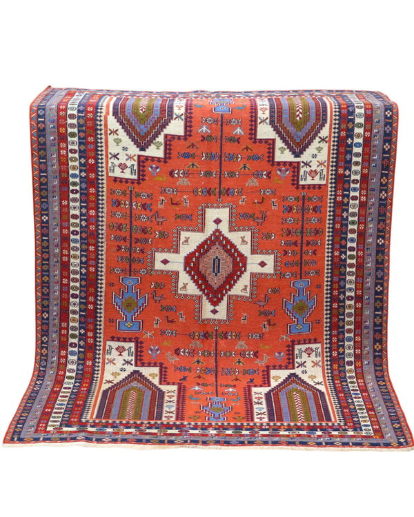 Tappeto Kilim 180x125 cm persiano tessuto a mano, con motivi geometrici tribali e medaglione centrale su fondo rosso mattone.