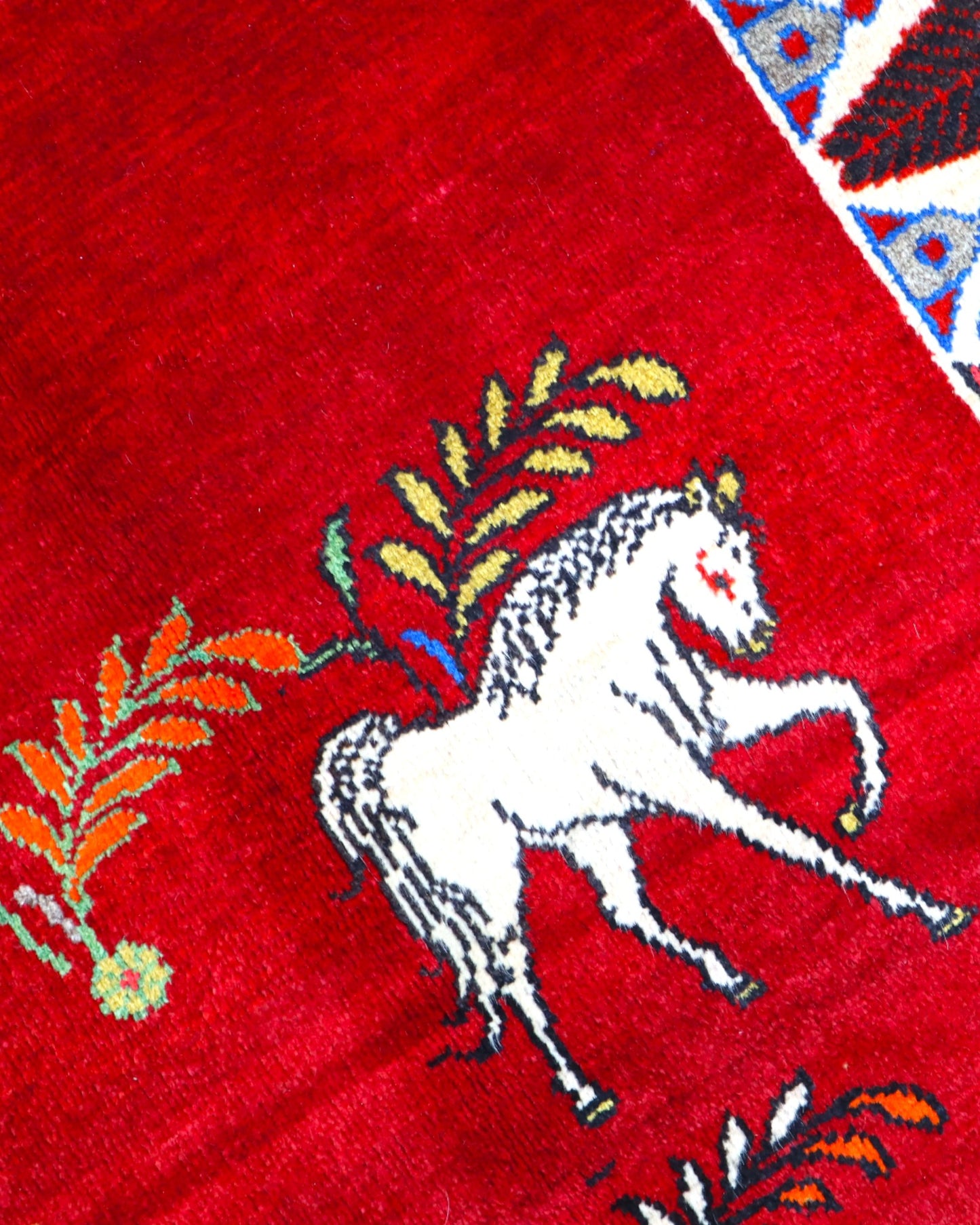 Tappeto Gashgai 185x111 cm annodato a mano, con cavalli stilizzati bianchi su fondo rosso e cornice geometrica multicolore.