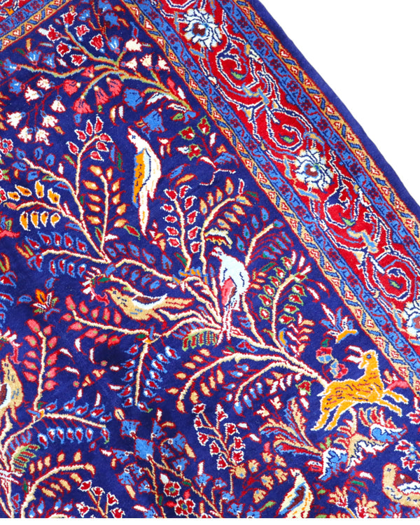 Tappeto Arak 210x126 cm persiano annodato a mano, con motivi floreali e animali su fondo blu intenso e cornice rossa decorata.