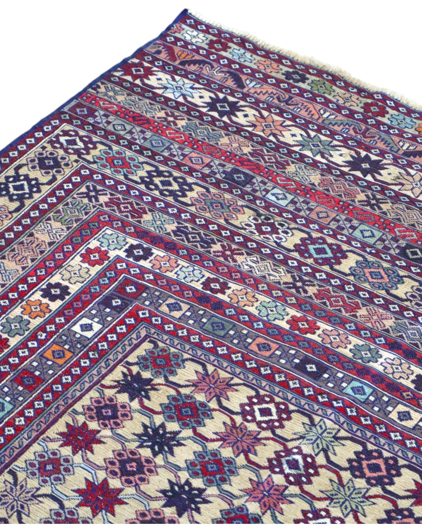 Tappeto Sumakh 180x130 cm con motivi geometrici e floreali in rosso, blu e crema su fondo beige.