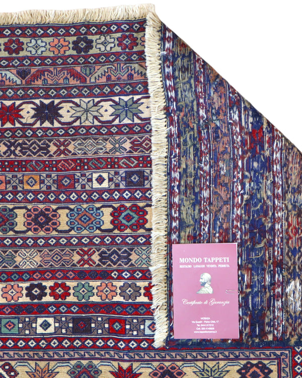 Tappeto Sumakh 180x130 cm con motivi geometrici e floreali in rosso, blu e crema su fondo beige.