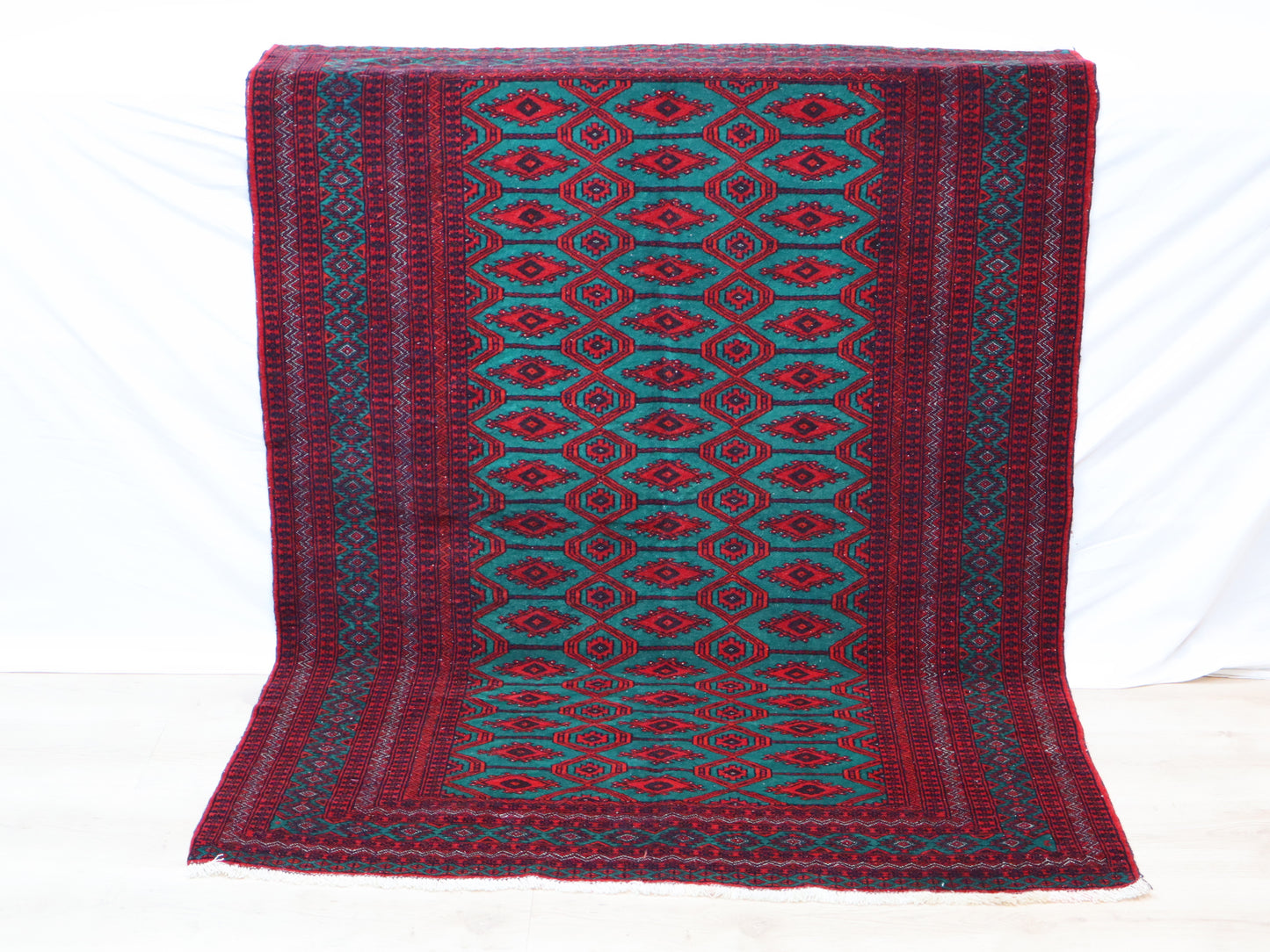 Tappeto Bukhara 172x126 cm annodato a mano, con motivi geometrici gul su fondo verde smeraldo e cornice rossa.