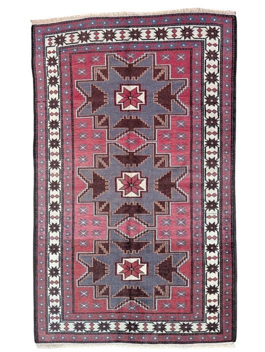 Tappeto Kazak 181x113 cm con motivo geometrico a stelle in rosso, blu e beige, annodato a mano con lana pregiata e ordito in cotone robusto.