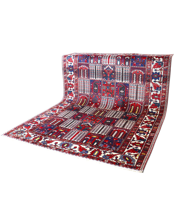 Tappeto persiano Bakhtiar 306x211 cm, motivo a pannelli con decorazioni floreali e geometriche in rosso, blu e avorio, annodato a mano in lana vegetale.