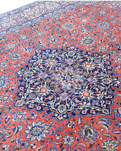 Tappeto persiano Saurk 345x240 cm, fondo rosso corallo con medaglione blu e cornice floreale chiara, annodato a mano in lana vegetale.