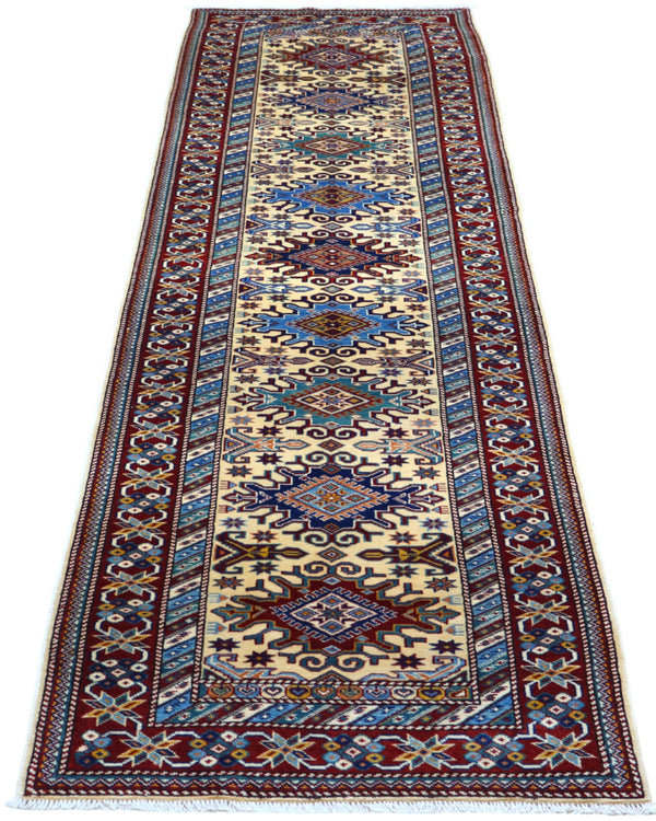 Elegante tappeto Shirvan annodato a mano in pura lana con colori vegetali. Dimensioni 301x83 cm, fondo beige con cornice rossa e motivi geometrici tradizionali afgani. Ideale per corridoi e ambienti raffinati.