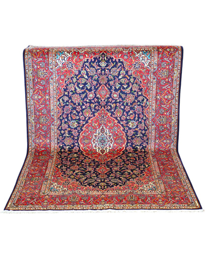 Tappeto Kashan persiano 225x142 cm, annodato a mano, fondo blu notte con motivo floreale e cornice rossa decorata, lana mista seta, certificato di autenticità incluso.