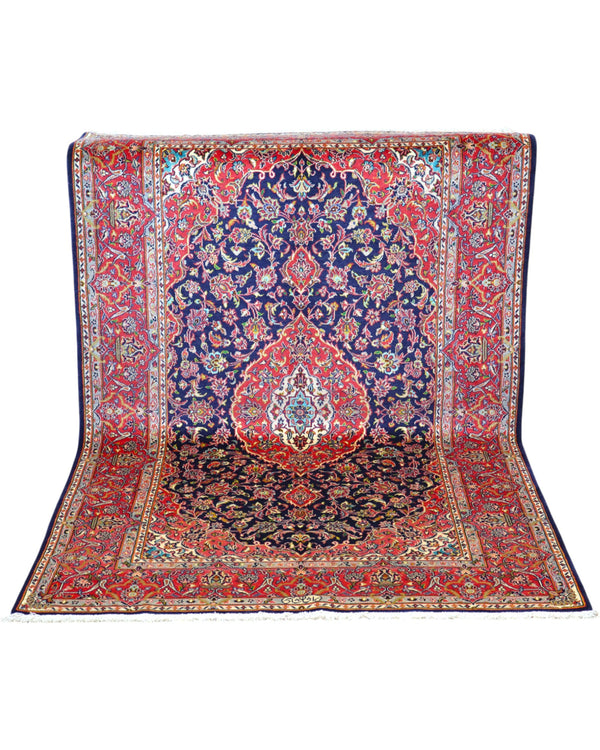 Tappeto Kashan persiano 225x142 cm, annodato a mano, fondo blu notte con motivo floreale e cornice rossa decorata, lana mista seta, certificato di autenticità incluso.
