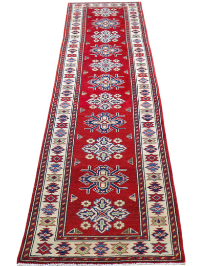 Passatoia Kazak annodata a mano (297x61 cm) in lana, con sfondo rosso melograno e bordo beige, con motivi geometrici afgani.

