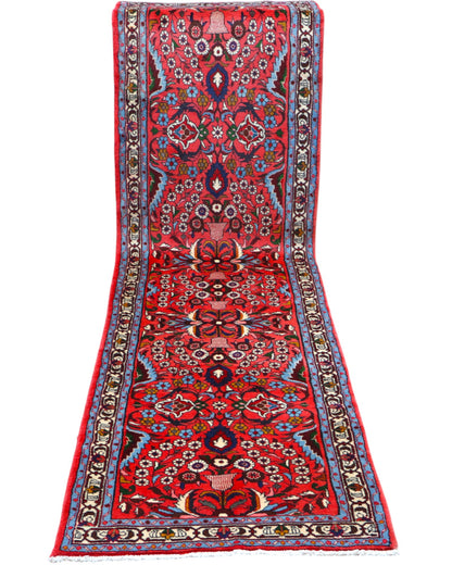 Passatoia persiana Lilian 297x78 cm annodata a mano in lana con colori vegetali, caratterizzata da un elegante fondo rosso antico e motivi decorativi.

