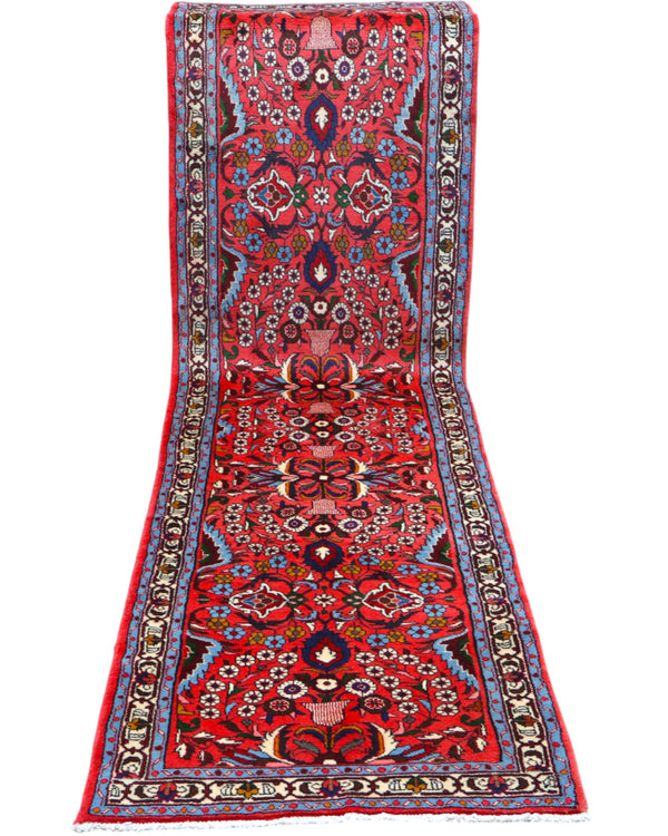 Passatoia persiana Lilian 297x78 cm annodata a mano in lana con colori vegetali, caratterizzata da un elegante fondo rosso antico e motivi decorativi.

