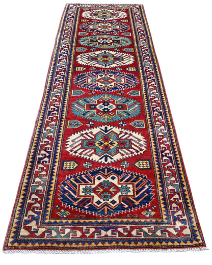Passatoia Kazak afgana 351x91 cm annodata a mano in lana, con un design audace caratterizzato da motivi geometrici su un fondo rosso intenso.