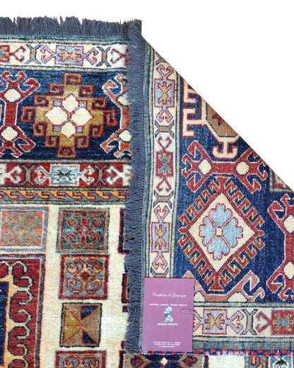 Tappeto Kazak 285x222 cm con fondo chiaro, motivi geometrici multicolore e bordure ricche, tramato ed annodato a mano, provenienza Caucaso.