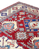 Tappeto Kazak 330x224 cm con fondo rosso, medaglione centrale avorio e motivi geometrici blu e azzurri, tramato ed annodato a mano, provenienza Caucaso.