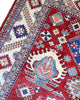 Tappeto Kazak 330x224 cm con fondo rosso, medaglione centrale avorio e motivi geometrici blu e azzurri, tramato ed annodato a mano, provenienza Caucaso.