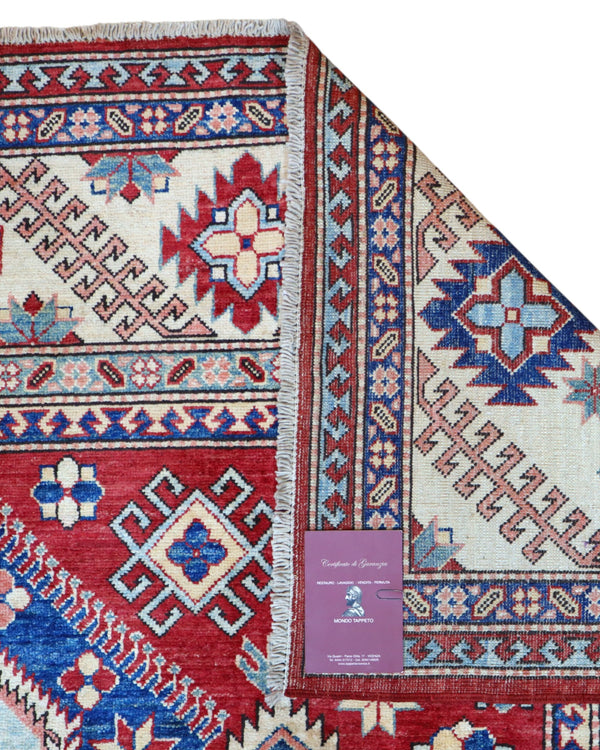 Tappeto Kazak 330x224 cm con fondo rosso, medaglione centrale avorio e motivi geometrici blu e azzurri, tramato ed annodato a mano, provenienza Caucaso.