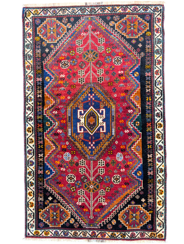 Tappeto Shiraz in rosso melograno con motivi geometrici e stilizzati, evocante un giardino persiano. Annodato a mano con lana e colori vegetali naturali in Persia.