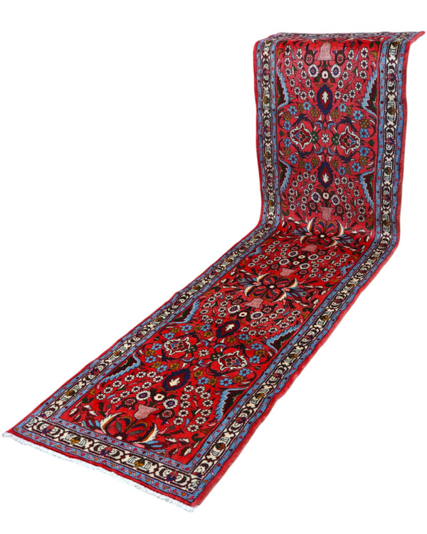 Passatoia persiana Lilian 297x78 cm annodata a mano in lana con colori vegetali, caratterizzata da un elegante fondo rosso antico e motivi decorativi.

