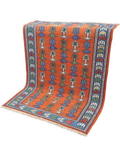 Tappeto Kilim 181x130 cm con motivi geometrici e figure stilizzate in blu, verde e rosso su fondo arancione e bordura decorata.