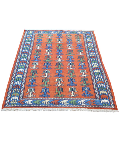 Tappeto Kilim 181x130 cm con motivi geometrici e figure stilizzate in blu, verde e rosso su fondo arancione e bordura decorata.