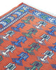 Tappeto Kilim 181x130 cm con motivi geometrici e figure stilizzate in blu, verde e rosso su fondo arancione e bordura decorata.