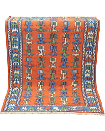 Tappeto Kilim 181x130 cm con motivi geometrici e figure stilizzate in blu, verde e rosso su fondo arancione e bordura decorata.