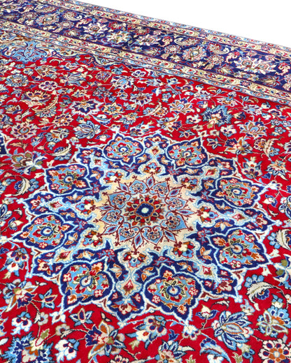 Tappeto persiano Najafabad 500x400 cm, fondo rosso con ampio medaglione centrale blu e cornice floreale scura, annodato a mano in lana vegetale.