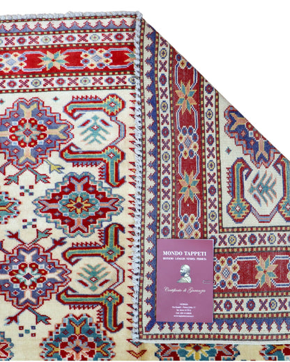 Tappeto Shirvan 165x122 cm con motivi geometrici e floreali in rosso, blu, verde e crema su fondo beige.