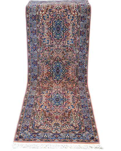 Tappeto persiano Kerman 247x77 cm, corridore con fondo rosa antico e motivi floreali blu e avorio, annodato a mano in lana vegetale.
