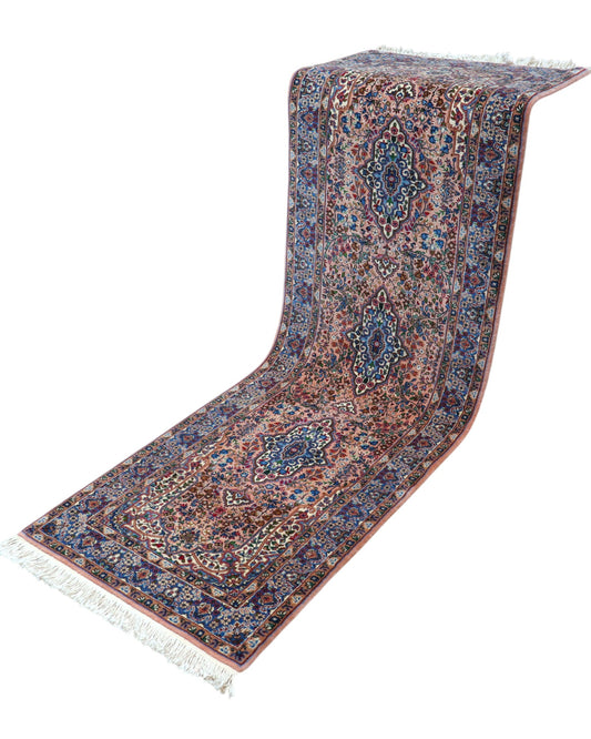 Tappeto persiano Kerman 247x77 cm, corridore con fondo rosa antico e motivi floreali blu e avorio, annodato a mano in lana vegetale.