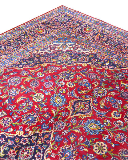 Tappeto persiano Kashan 400x290 cm, fondo rosso con medaglione centrale blu e avorio, cornice scura floreale, annodato a mano in lana vegetale.
