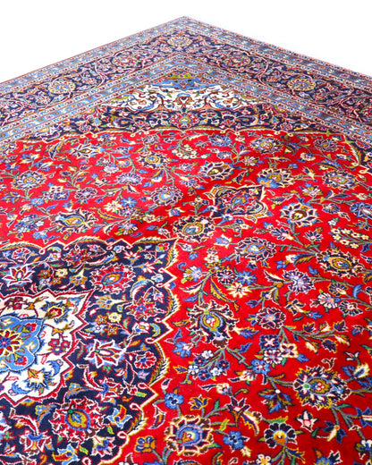 Tappeto persiano Kashan 402x297 cm, fondo rosso con medaglione centrale blu e avorio, annodato a mano in lana vegetale.