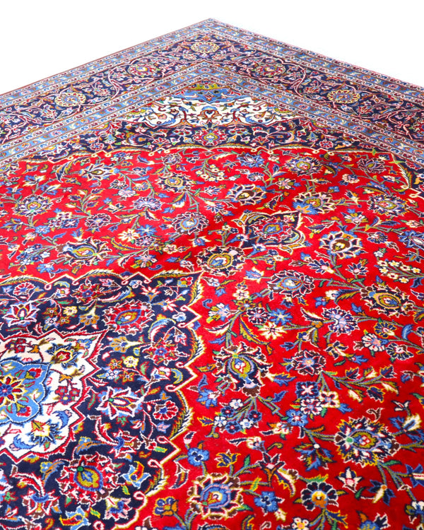 Tappeto persiano Kashan 402x297 cm, fondo rosso con medaglione centrale blu e avorio, annodato a mano in lana vegetale.