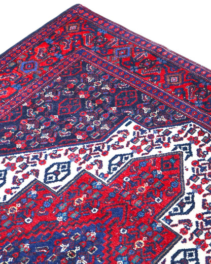 Tappeto Senneh 174x122 cm, annodato a mano, con grande medaglione geometrico centrale e motivi floreali su campo rosso e blu.