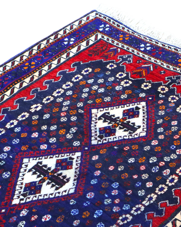 Tappeto Balucestan 215x100 cm annodato a mano, con sequenza di rombi centrali su fondo blu notte e bordi rosso granata.