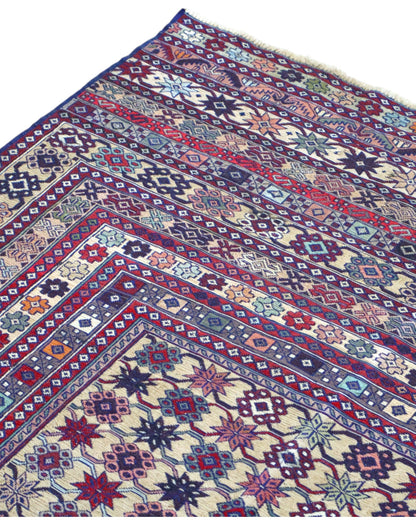 Tappeto Sumakh 180x130 cm con motivi geometrici e floreali in rosso, blu e crema su fondo beige.