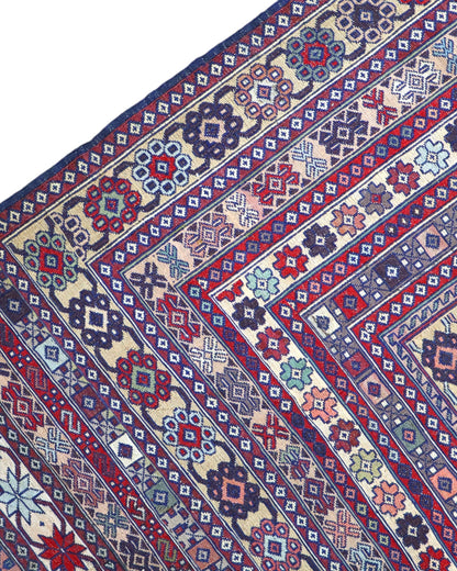 Tappeto Sumakh 180x130 cm con motivi geometrici e floreali in rosso, blu e crema su fondo beige.