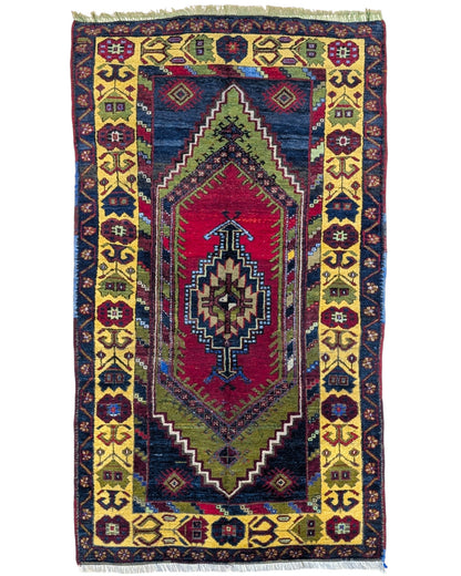 Tappeto Turco 179x103 cm, annodato a mano, con medaglione centrale geometrico rosso, motivi tribali e bordura gialla decorata.