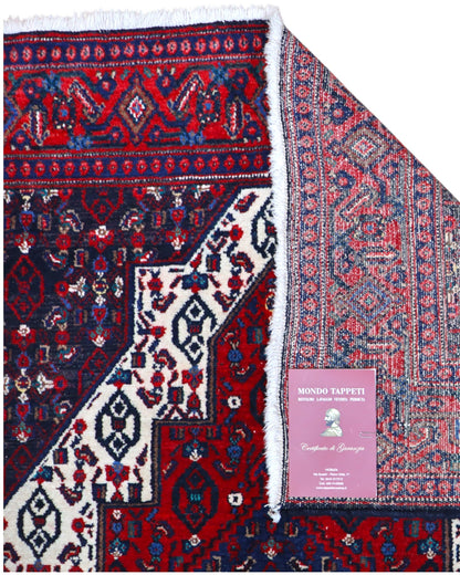 Tappeto Senneh 174x122 cm, annodato a mano, con grande medaglione geometrico centrale e motivi floreali su campo rosso e blu.